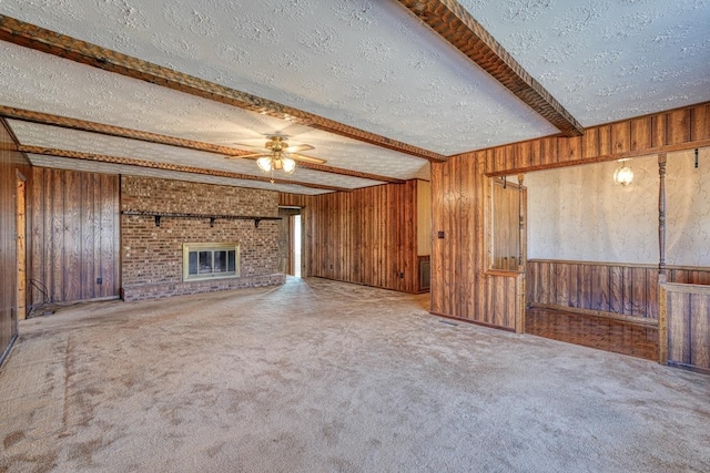 unfurnished living room featuring beam ceiling, carpet flooring, ceiling fan, a brick fireplace, and a textured ceiling