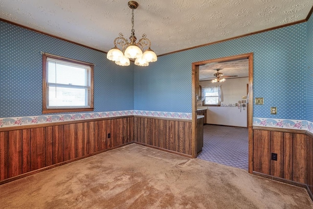 unfurnished dining area with carpet flooring, a textured ceiling, ceiling fan with notable chandelier, and ornamental molding