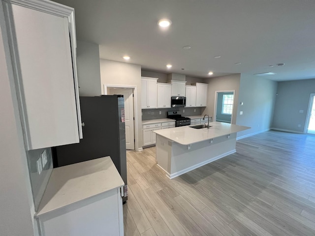 kitchen featuring stainless steel appliances, white cabinetry, a center island with sink, and sink