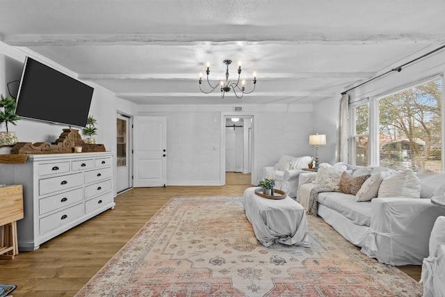 living room featuring a chandelier, light wood-type flooring, beamed ceiling, and brick wall