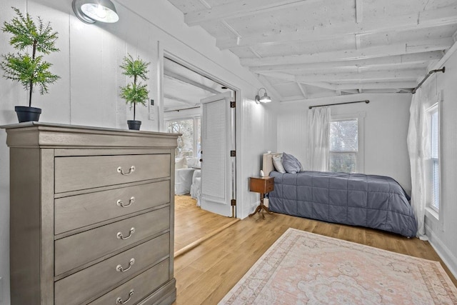 bedroom featuring vaulted ceiling with beams, multiple windows, and light wood-type flooring