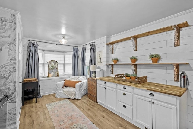 interior space featuring wooden counters, wooden walls, crown molding, light hardwood / wood-style flooring, and white cabinets