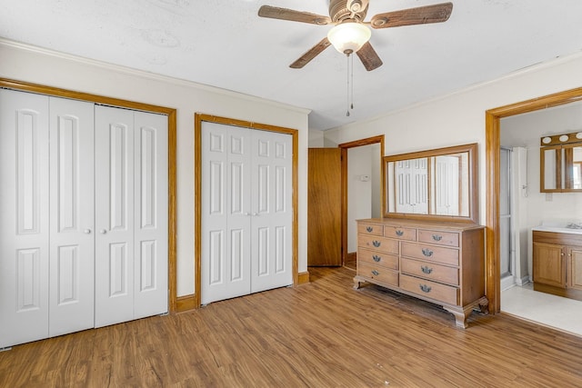 unfurnished bedroom with light wood-type flooring, connected bathroom, two closets, and ceiling fan