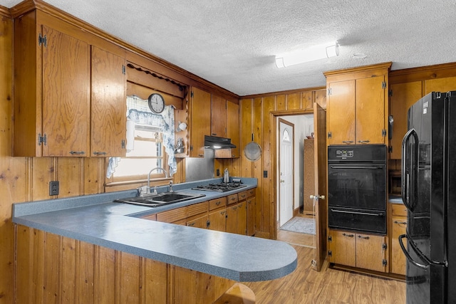 kitchen with black appliances, sink, wooden walls, light hardwood / wood-style flooring, and kitchen peninsula