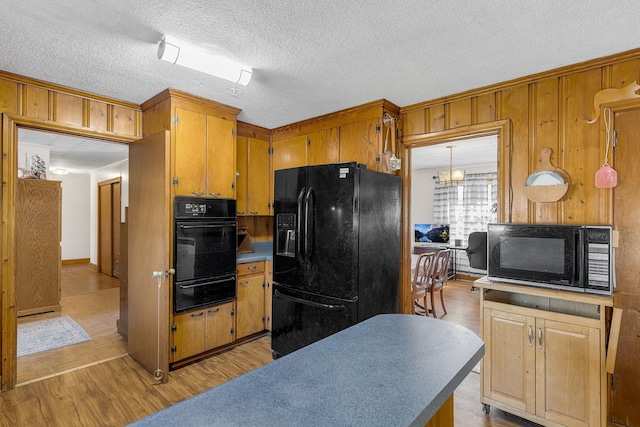 kitchen with black appliances, decorative light fixtures, wood walls, and light hardwood / wood-style floors