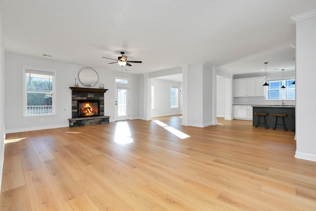 unfurnished living room featuring light hardwood / wood-style floors, ceiling fan, sink, and a fireplace