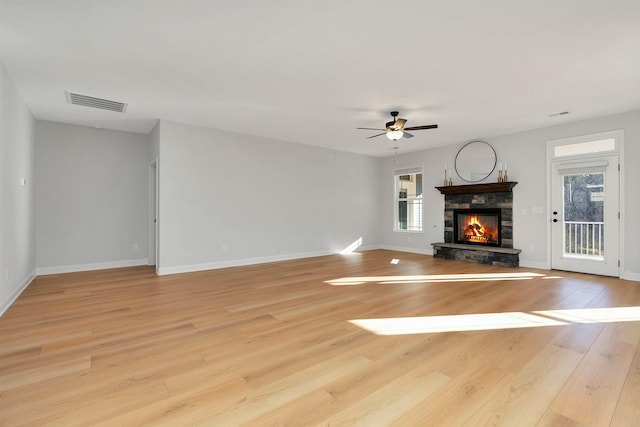 unfurnished living room featuring light wood-type flooring, ceiling fan, and a stone fireplace