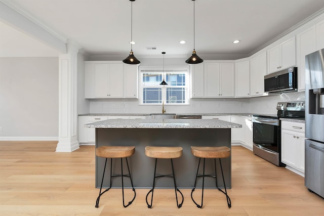 kitchen featuring stainless steel appliances, white cabinets, a center island, and light stone countertops