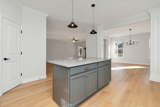 kitchen featuring light stone counters, hanging light fixtures, a kitchen island, ceiling fan with notable chandelier, and ornamental molding