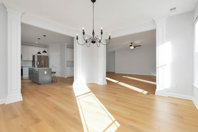 unfurnished dining area featuring ceiling fan with notable chandelier, light wood-type flooring, and ornate columns