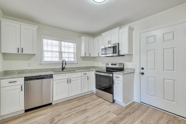 kitchen featuring sink, light stone counters, light wood-type flooring, white cabinetry, and stainless steel appliances