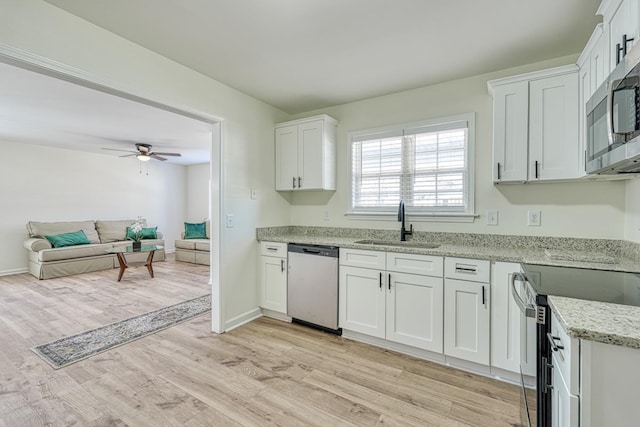 kitchen with light wood-type flooring, stainless steel appliances, light stone counters, white cabinets, and sink