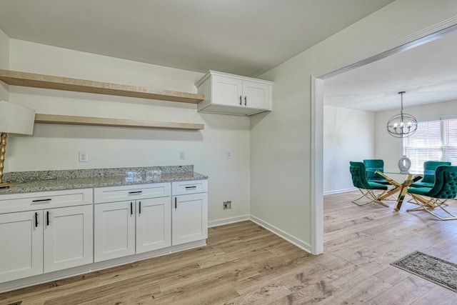 kitchen featuring white cabinetry, hanging light fixtures, light stone countertops, a notable chandelier, and light hardwood / wood-style floors