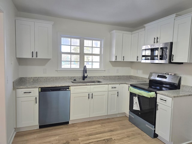 kitchen featuring appliances with stainless steel finishes, sink, light stone counters, light wood-type flooring, and white cabinetry