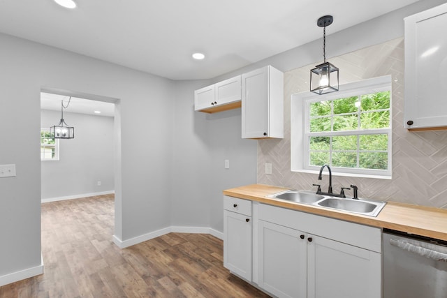 kitchen with stainless steel dishwasher, hanging light fixtures, butcher block counters, white cabinets, and sink