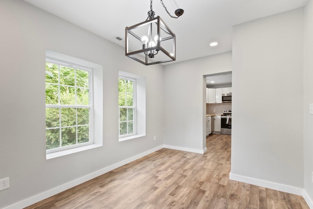 unfurnished dining area with an inviting chandelier and light wood-type flooring