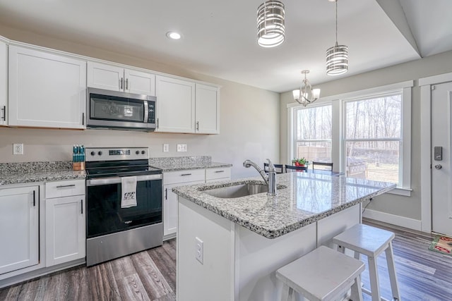 kitchen featuring sink, white cabinetry, wood-type flooring, hanging light fixtures, and appliances with stainless steel finishes