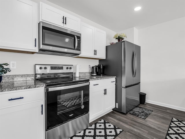 kitchen with white cabinets, stainless steel appliances, dark stone countertops, and dark wood-type flooring