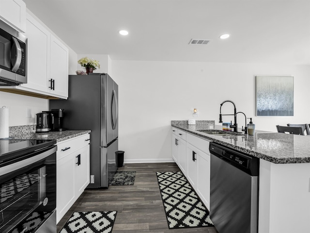 kitchen with appliances with stainless steel finishes, white cabinetry, dark stone countertops, and sink