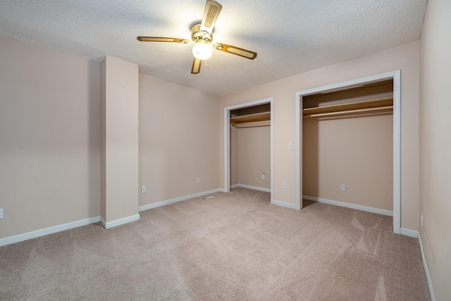 unfurnished bedroom with light carpet, a textured ceiling, ceiling fan, and two closets