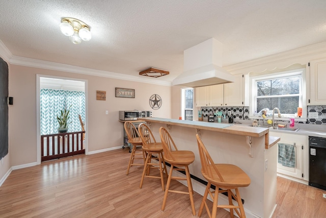 kitchen with dishwasher, light hardwood / wood-style floors, a kitchen bar, decorative backsplash, and sink