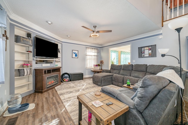 living room featuring a textured ceiling, ceiling fan, wood-type flooring, built in shelves, and crown molding