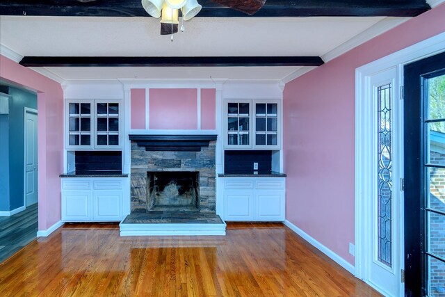 unfurnished living room featuring a fireplace, ceiling fan, wood-type flooring, crown molding, and beam ceiling