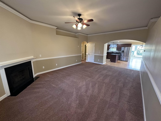 unfurnished living room with dark carpet, ceiling fan, and ornamental molding