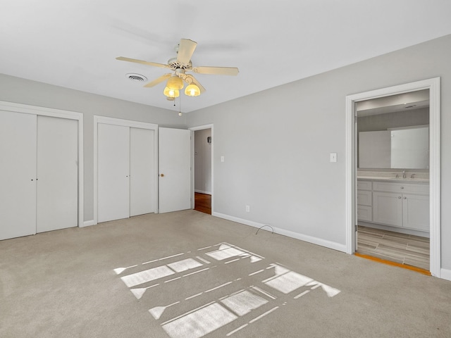 unfurnished bedroom with light carpet, ceiling fan, multiple closets, sink, and ensuite bathroom