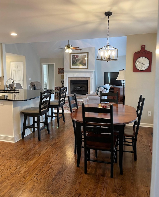 dining room featuring sink, ceiling fan with notable chandelier, a fireplace, and dark wood-type flooring