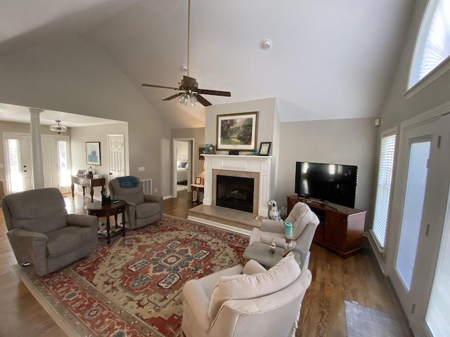 living room featuring vaulted ceiling, ornate columns, a tiled fireplace, ceiling fan, and wood-type flooring