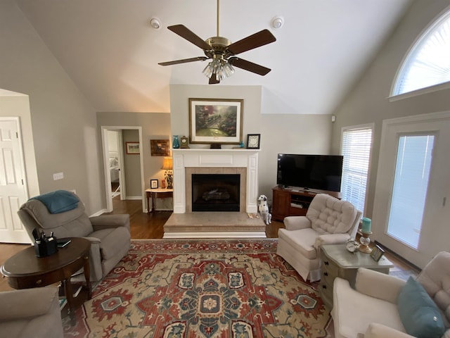 living room with a tiled fireplace, ceiling fan, vaulted ceiling, and dark wood-type flooring