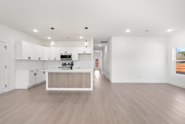 kitchen with a center island with sink, light hardwood / wood-style floors, pendant lighting, decorative backsplash, and white cabinetry