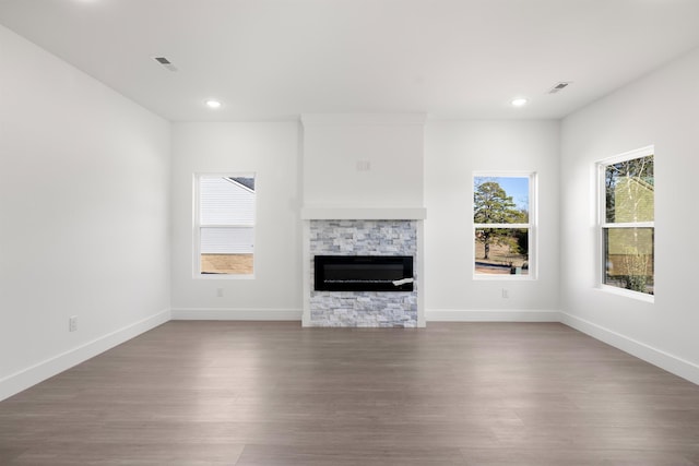 unfurnished living room featuring hardwood / wood-style flooring and a stone fireplace