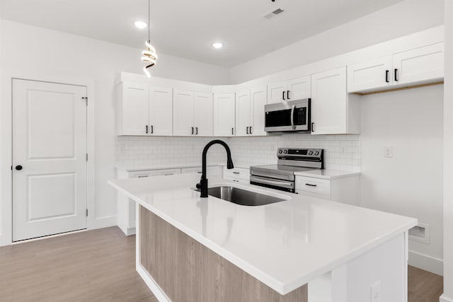 kitchen with white cabinets, stainless steel appliances, and an island with sink