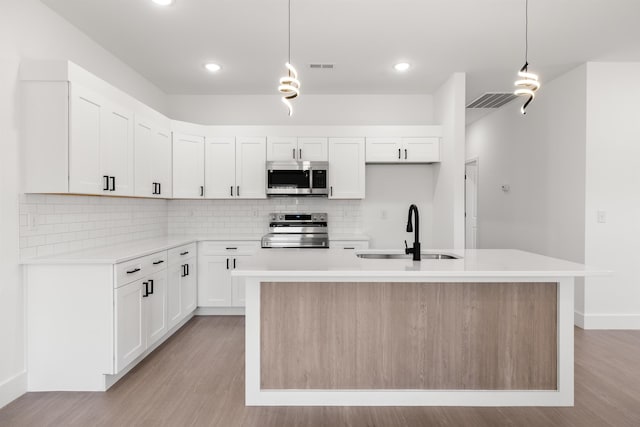 kitchen with pendant lighting, a center island with sink, white cabinets, appliances with stainless steel finishes, and sink