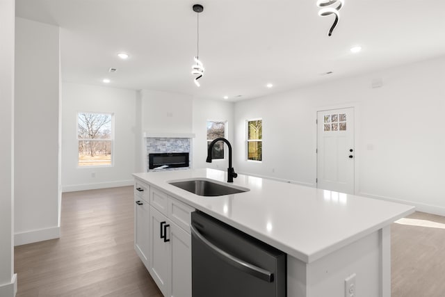 kitchen featuring stainless steel dishwasher, decorative light fixtures, an island with sink, white cabinetry, and sink