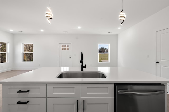 kitchen featuring dishwasher, a center island with sink, light hardwood / wood-style floors, hanging light fixtures, and sink