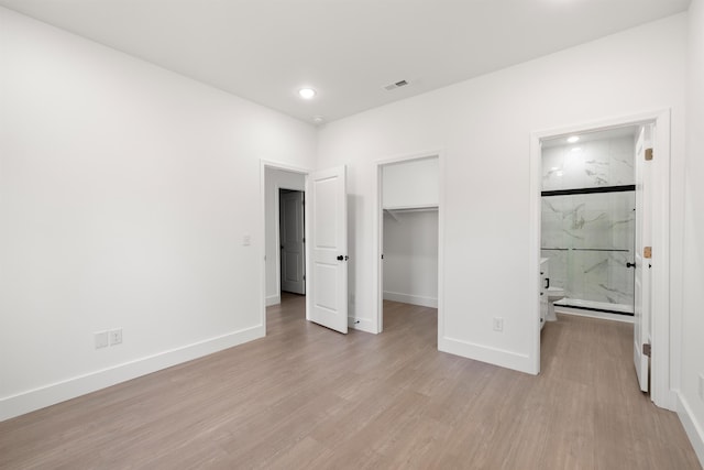 unfurnished bedroom with light hardwood / wood-style flooring, a spacious closet, ensuite bathroom, and a closet