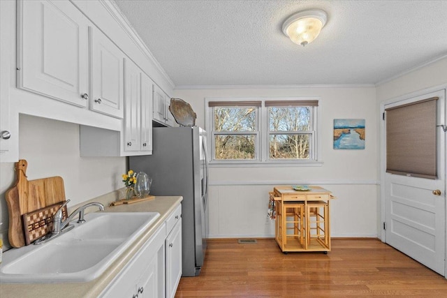 kitchen featuring light hardwood / wood-style flooring, stainless steel fridge with ice dispenser, white cabinets, ornamental molding, and sink