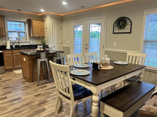 dining area featuring sink, ornamental molding, french doors, and light wood-type flooring