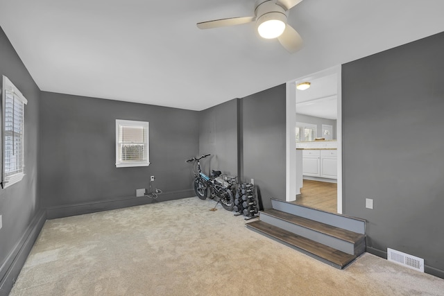 workout area featuring light colored carpet, ceiling fan, and plenty of natural light