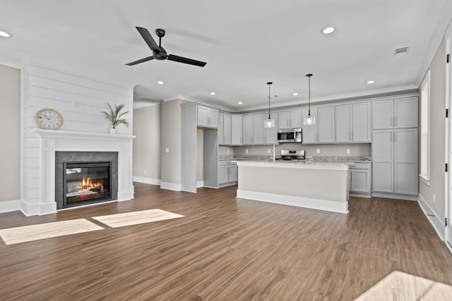 kitchen with gray cabinets, pendant lighting, light stone countertops, a kitchen island with sink, and appliances with stainless steel finishes