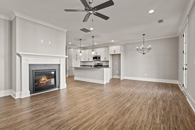 unfurnished living room with ceiling fan with notable chandelier, wood-type flooring, and ornamental molding