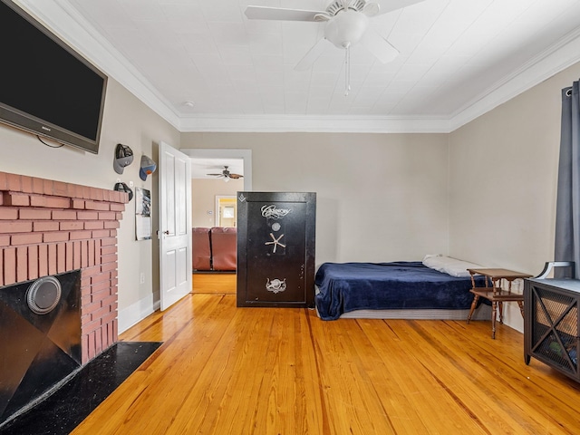 bedroom with ceiling fan, light hardwood / wood-style floors, a brick fireplace, and crown molding