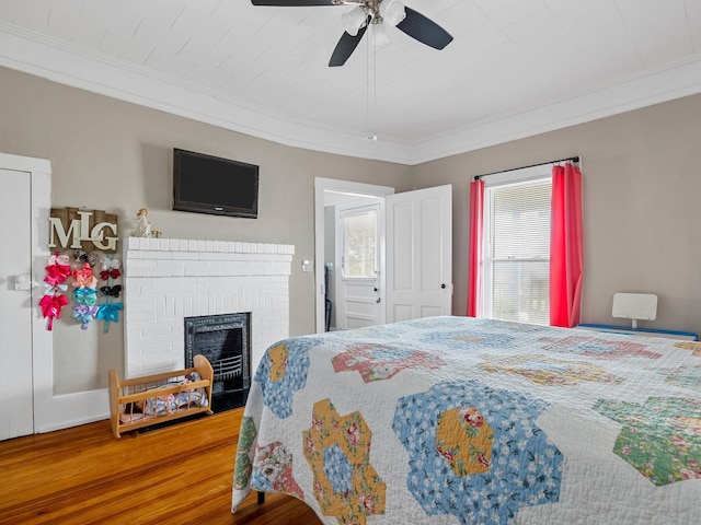 bedroom featuring ornamental molding, ceiling fan, a fireplace, and hardwood / wood-style floors