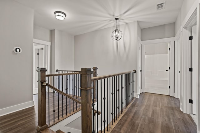 hallway with dark wood-type flooring and an inviting chandelier