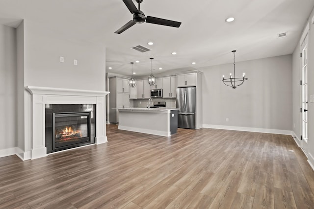 unfurnished living room featuring sink, ceiling fan with notable chandelier, and wood-type flooring