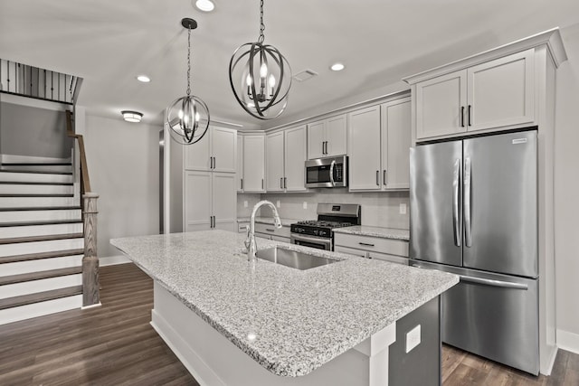 kitchen featuring sink, hanging light fixtures, light stone countertops, a center island with sink, and appliances with stainless steel finishes