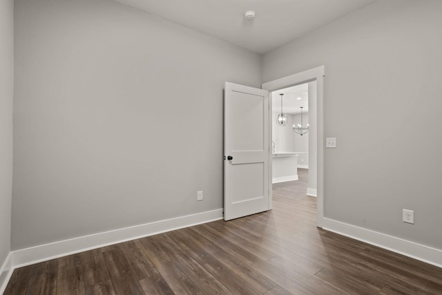 empty room with a notable chandelier and dark hardwood / wood-style floors